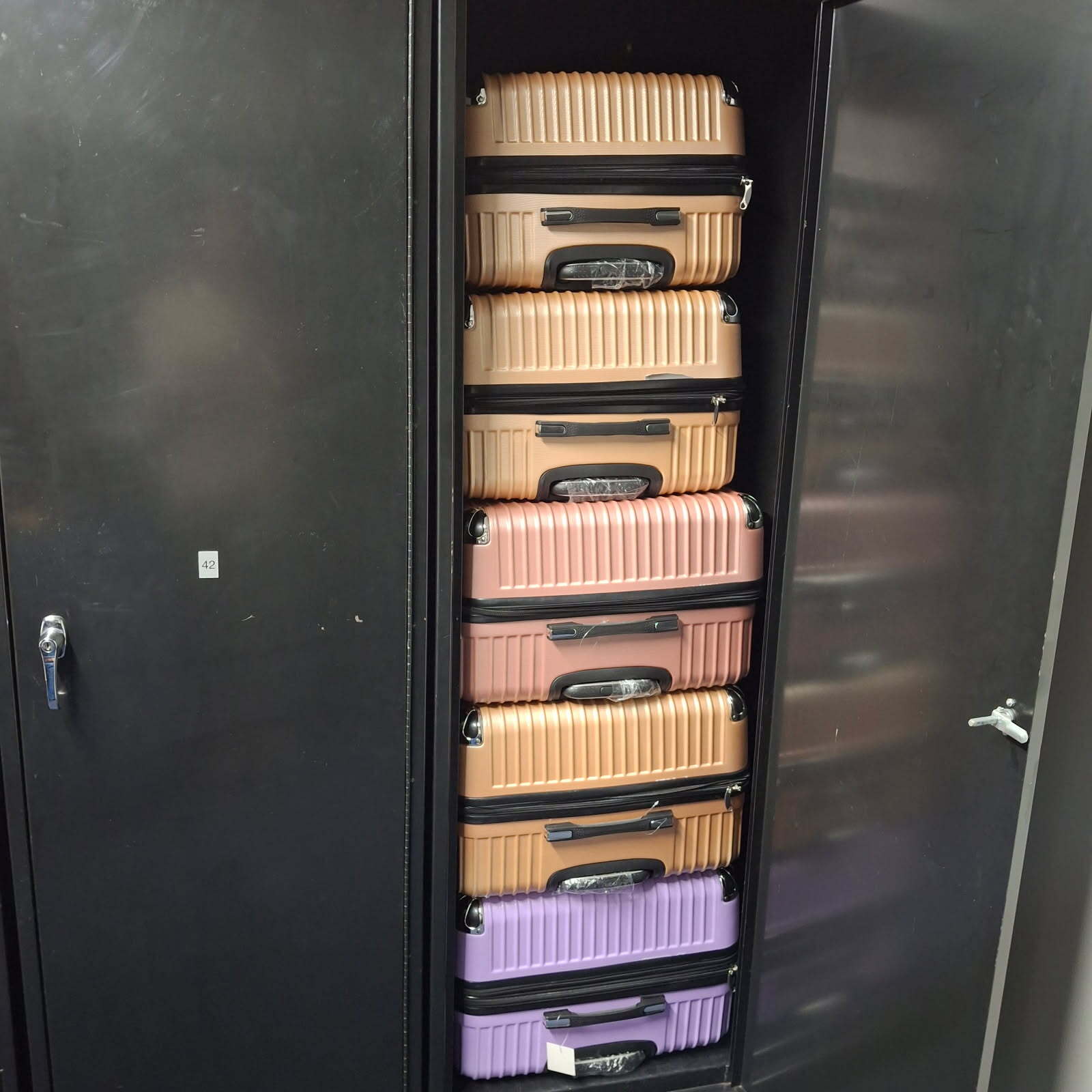 Stack of colorful luggage suitcases stored vertically in narrow wall closet.